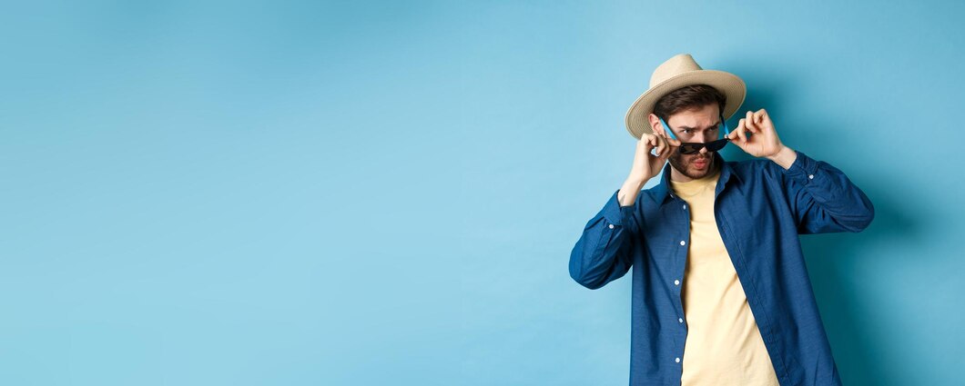 Man wearing a light-colored hat and sunglasses against a blue background